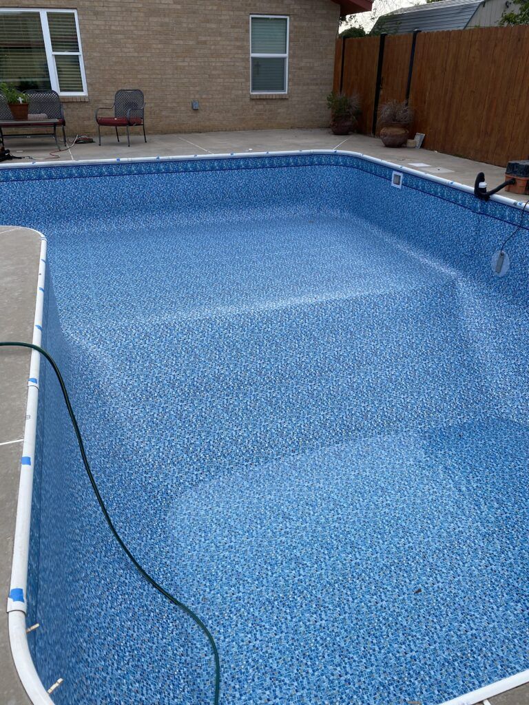 Empty rectangular swimming pool with blue mosaic-patterned liner, surrounded by concrete deck.
