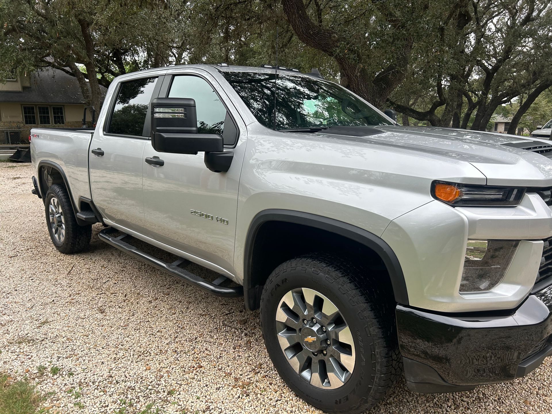 Silver Chevrolet pickup truck parked on gravel near a house with trees.