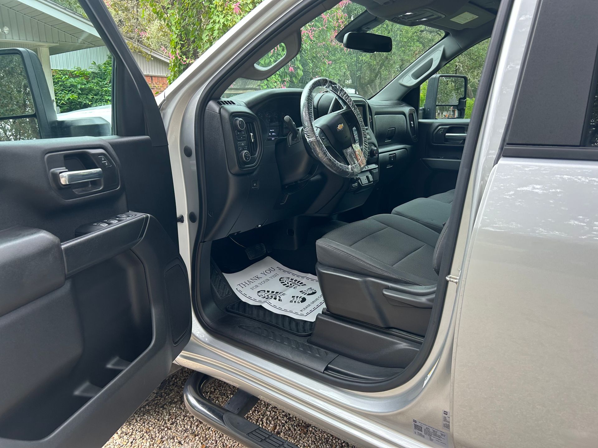 Silver truck interior; open door reveals driver's seat, steering wheel, and floor mat.