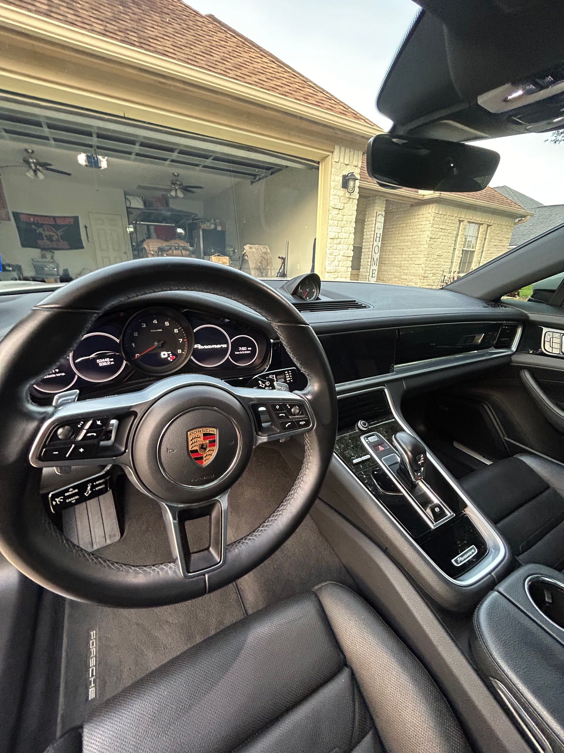 Interior of a Porsche Panamera, black leather seats, steering wheel, and console. Garage in background.