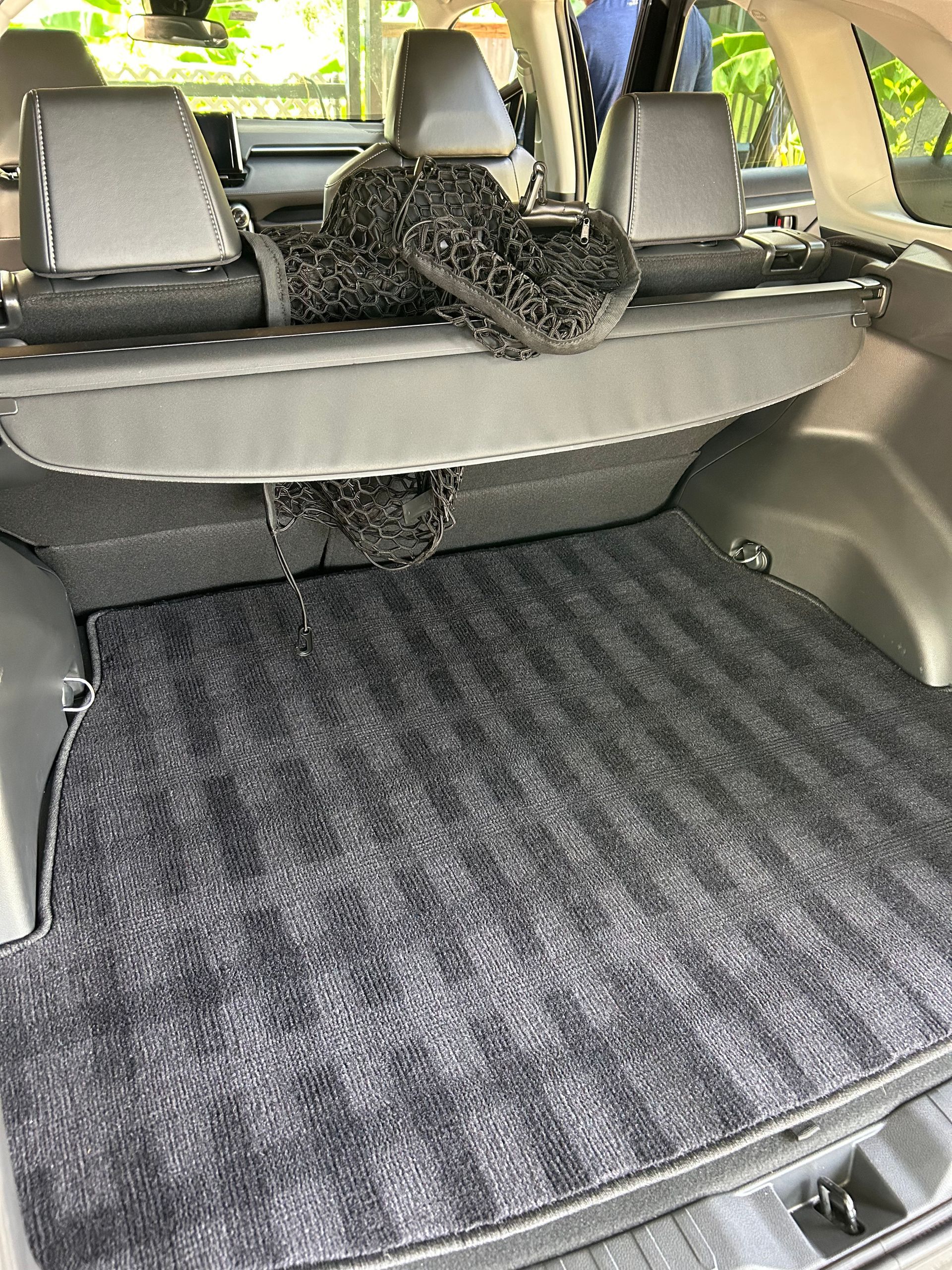 Car trunk with a dark gray patterned floor mat and a folded car cover.