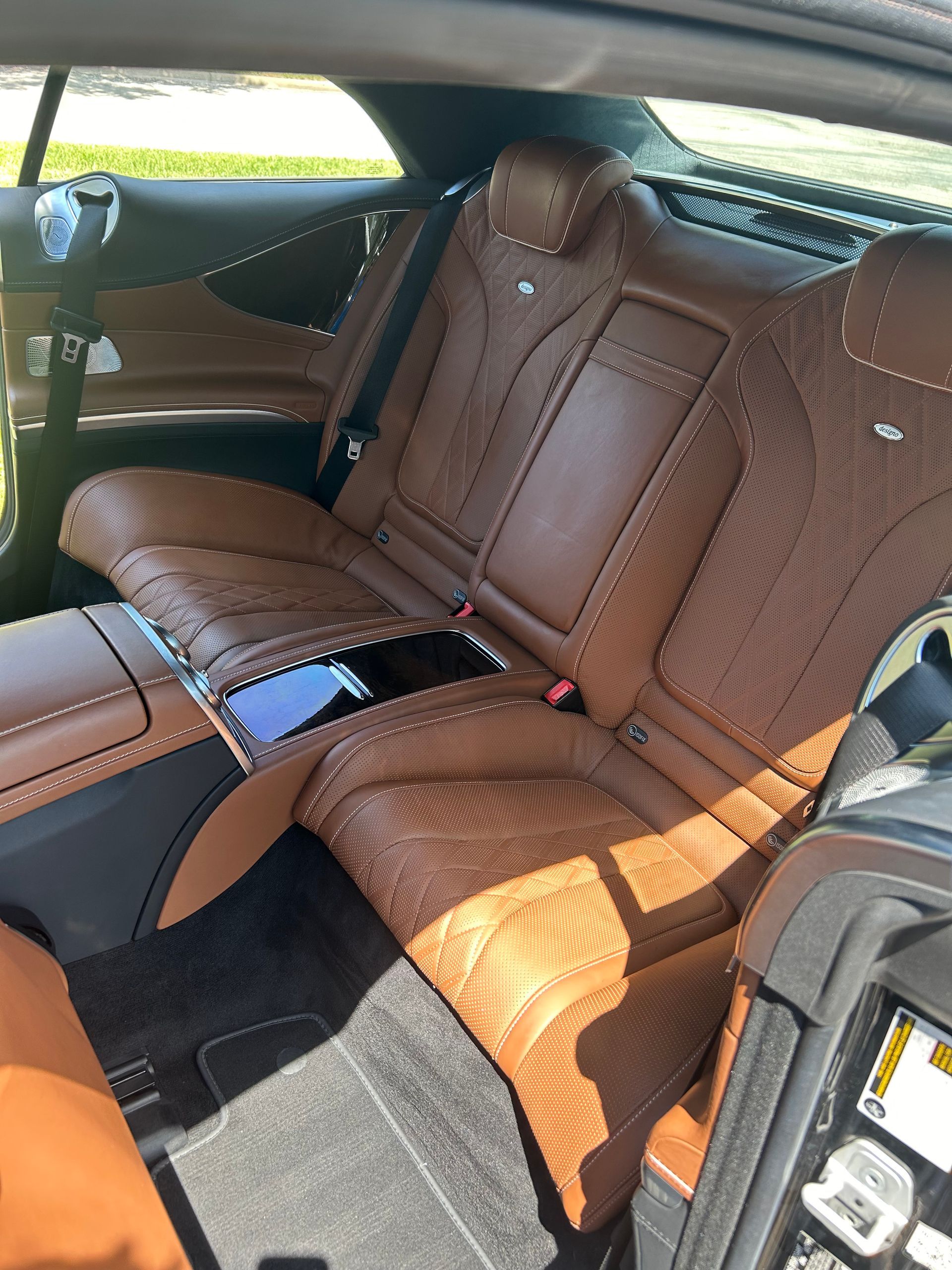 Brown leather car seats, detailed stitching, center console, dark interior, rear view.