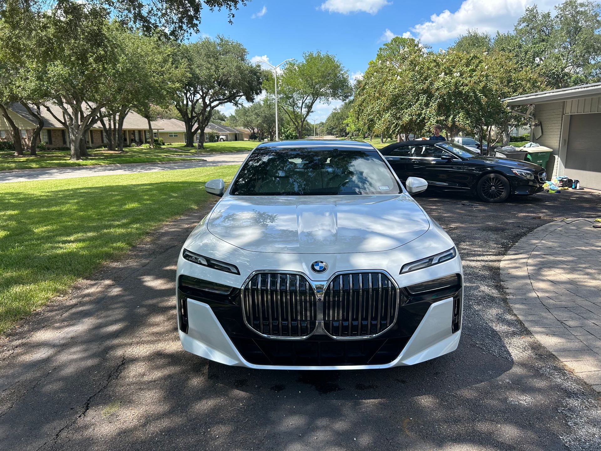 White BMW sedan parked on a driveway; black grill, sunny day.