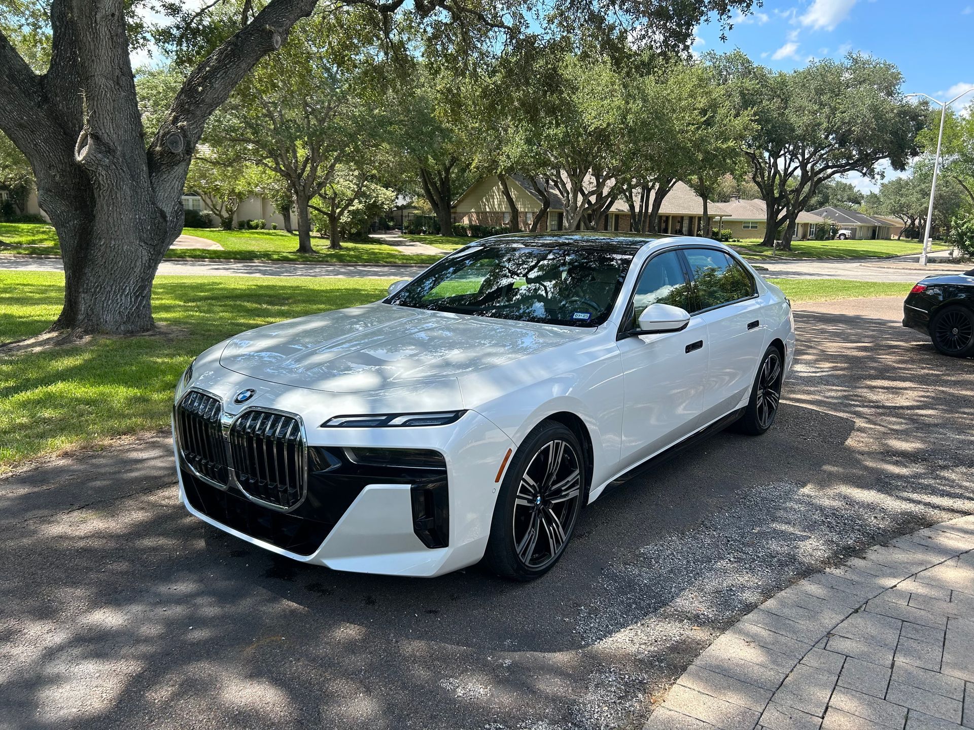 White BMW sedan parked on a paved driveway under trees on a sunny day.