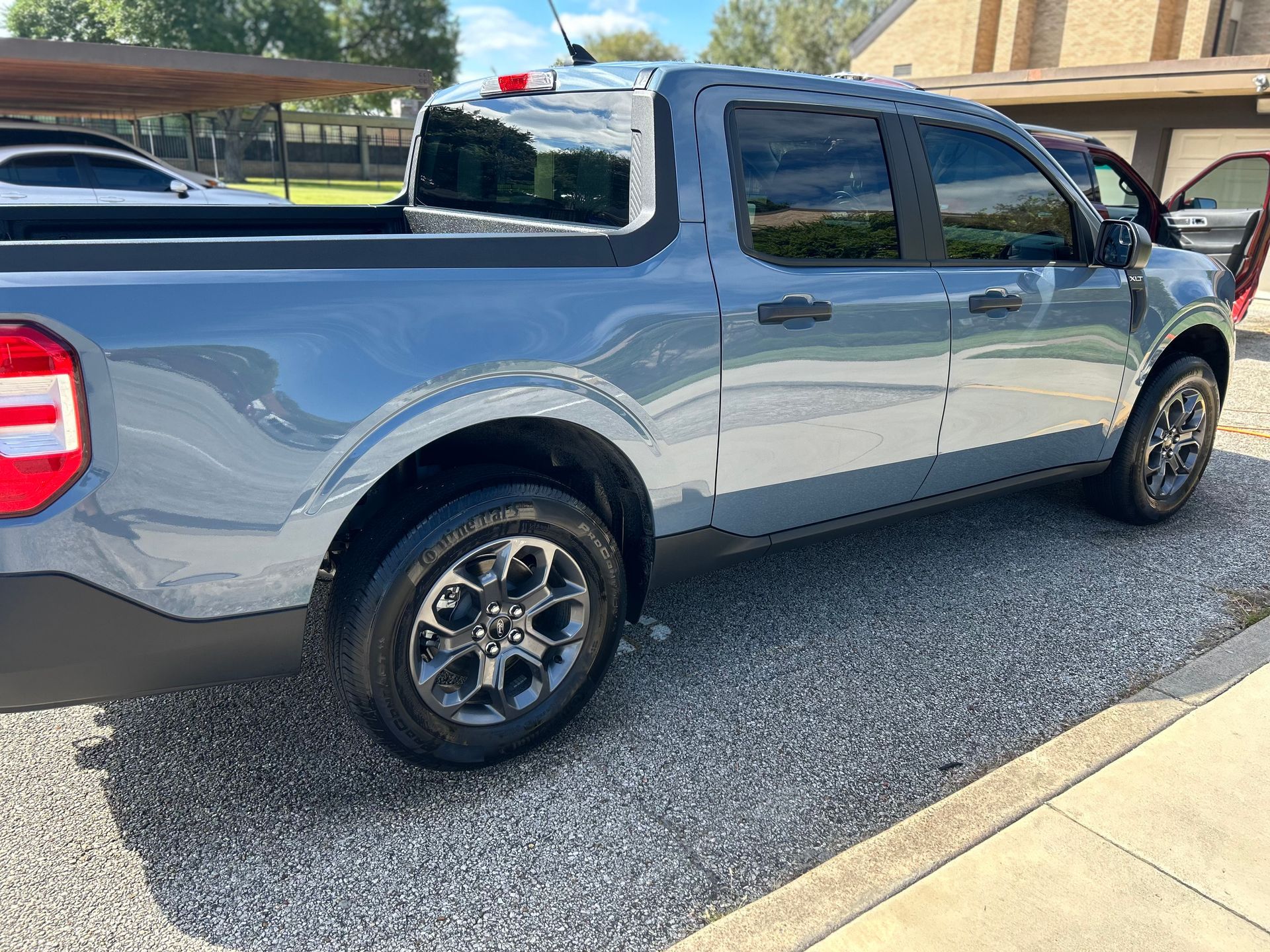 Gray Ford Maverick pickup truck parked on gravel, sunny day.