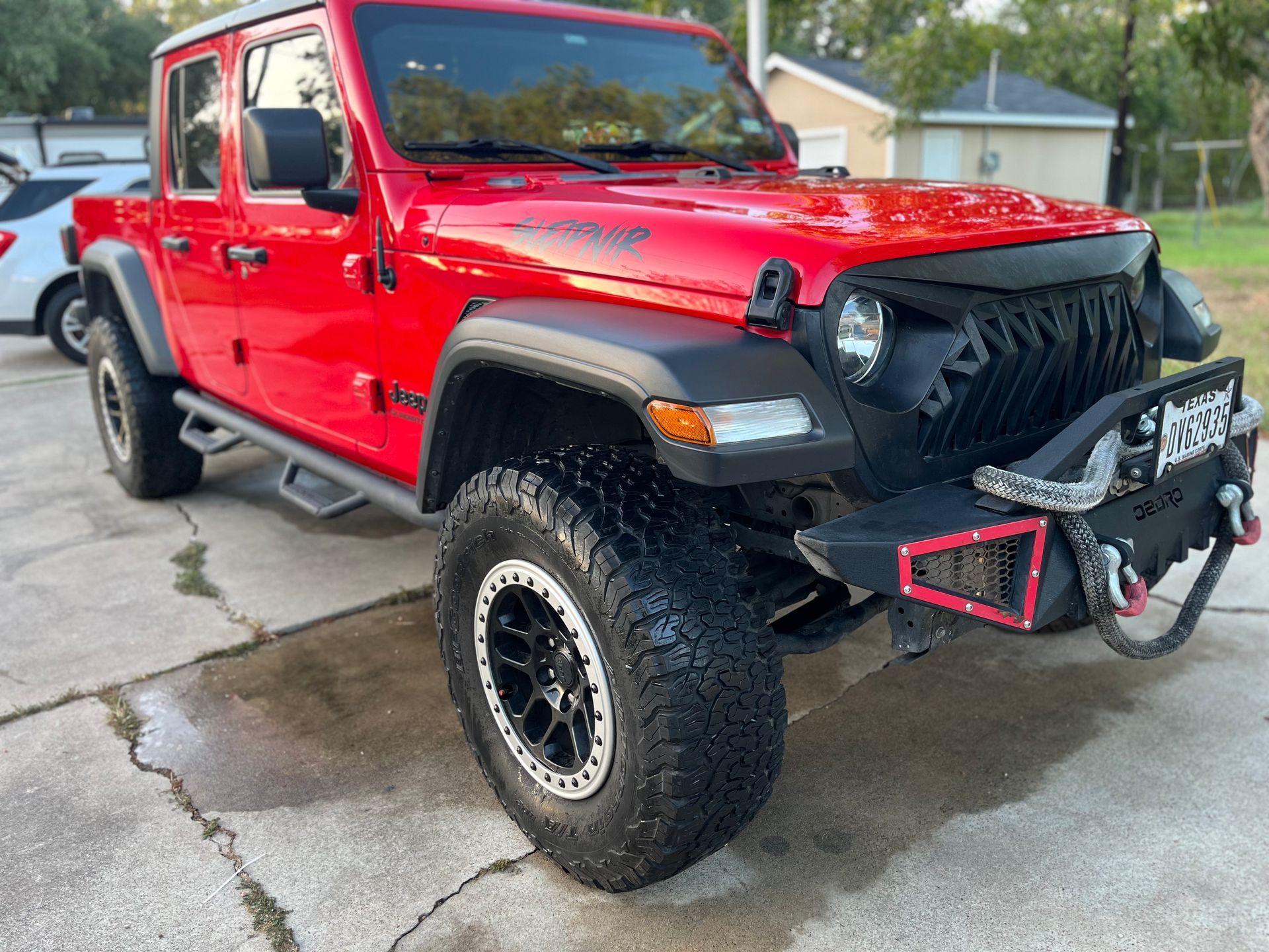 Red Jeep Gladiator, black front bumper, on a paved driveway.