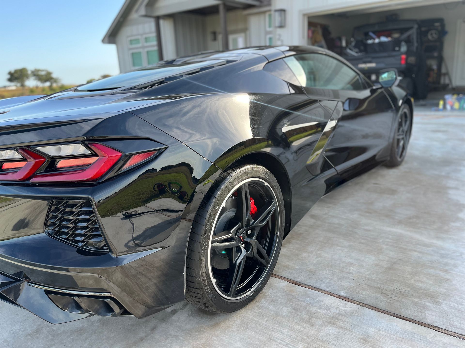 Black Corvette parked in front of a house with a garage. Red brake calipers and black rims are visible.