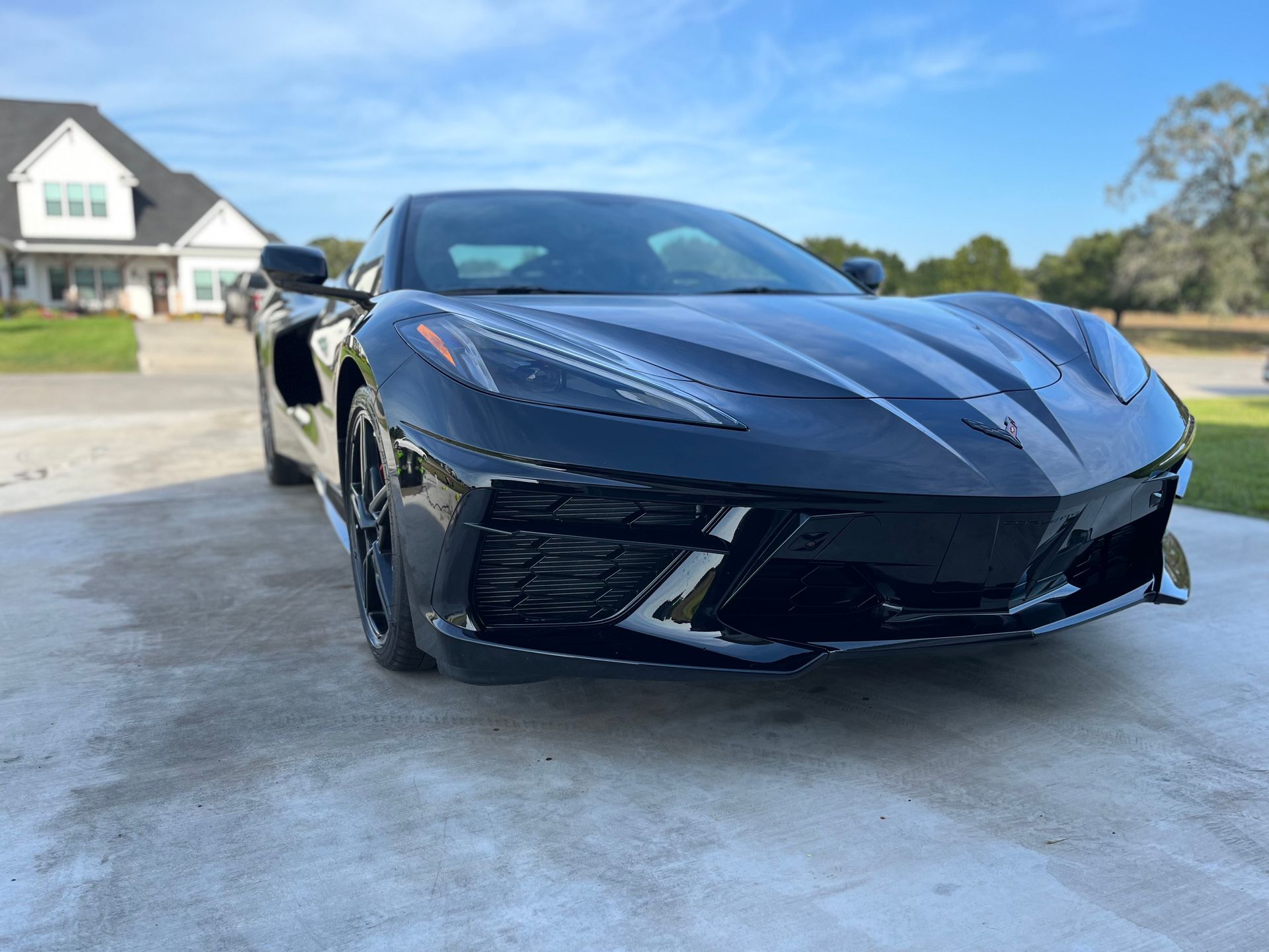 Black Corvette sports car parked on a driveway in front of a house on a sunny day.