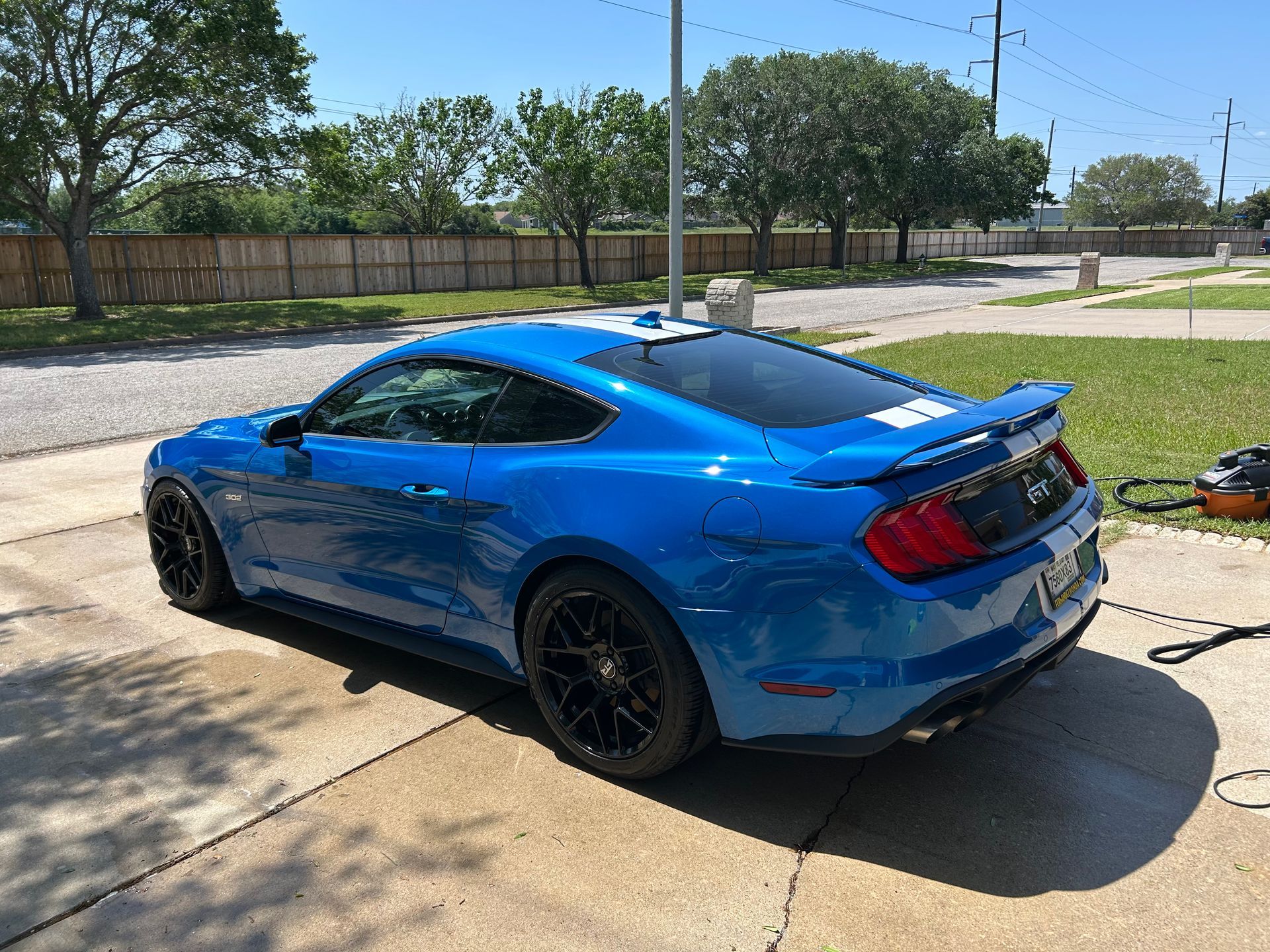 Blue Ford Mustang parked on a driveway with black rims under a sunny sky.