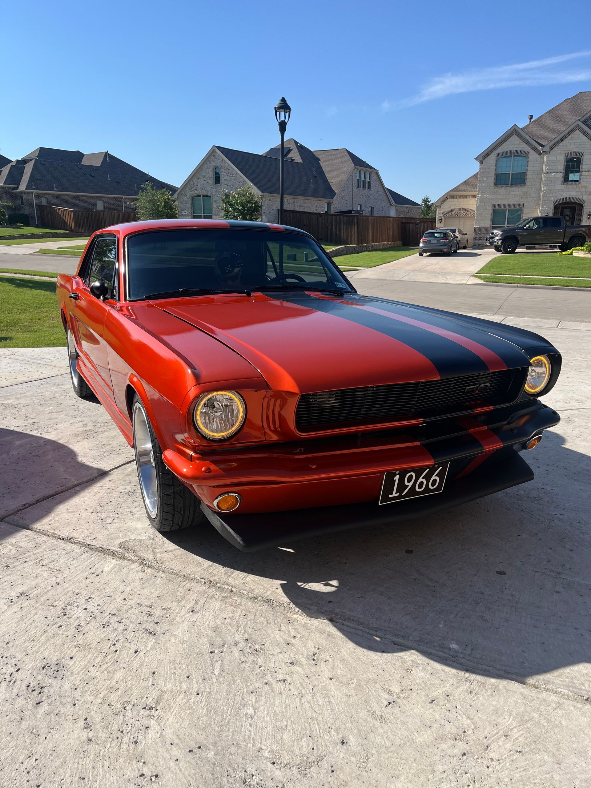 Classic red and black 1966 Ford Mustang on a sunny driveway.