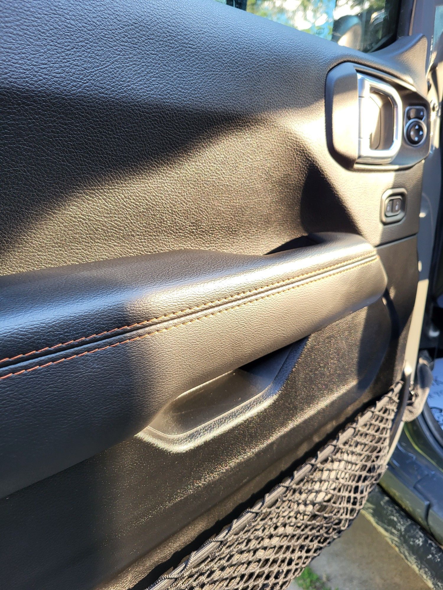 Black Jeep door panel with textured surface, black armrest, and cargo net.