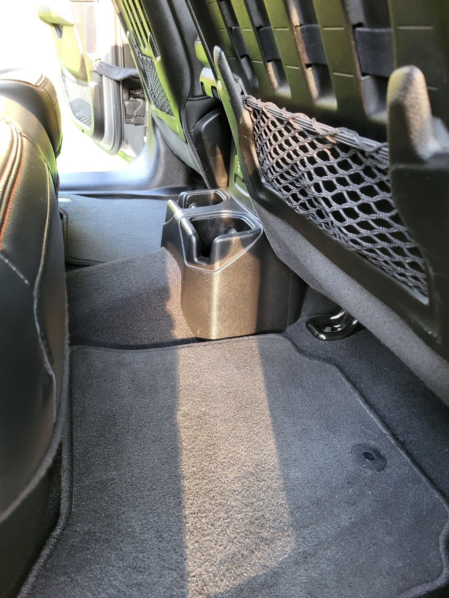 Rear seat cup holders in a vehicle, carpeted floor, black interior, sunlight.