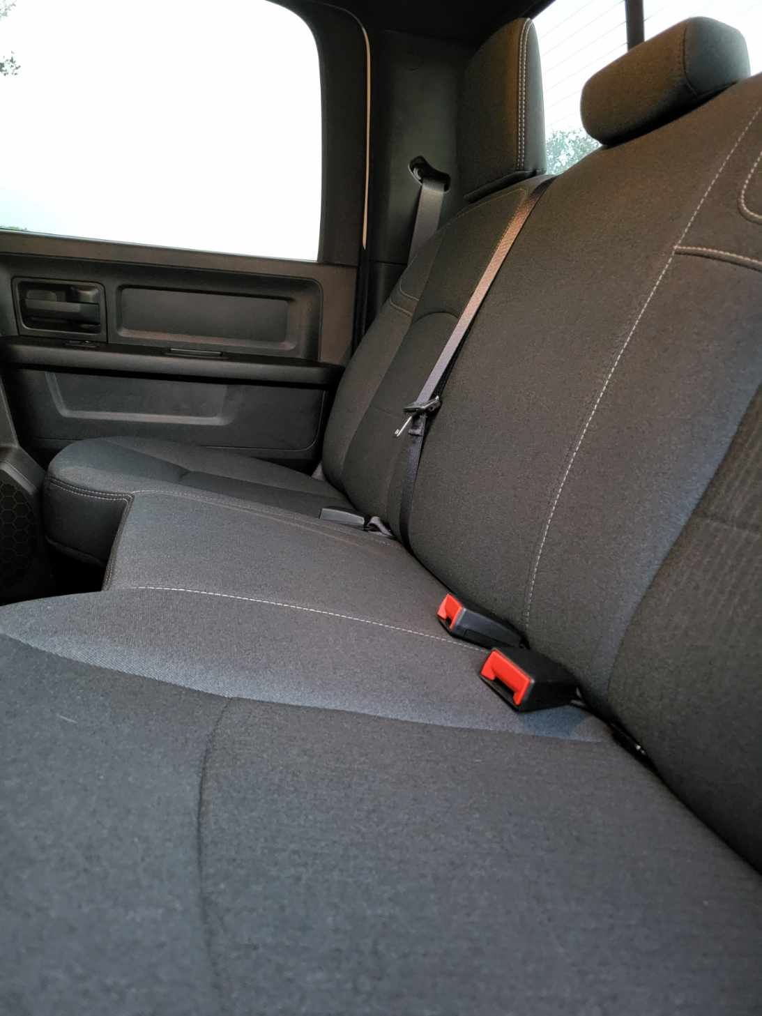 Back seat of a black pickup truck, with seatbelts and headrests.