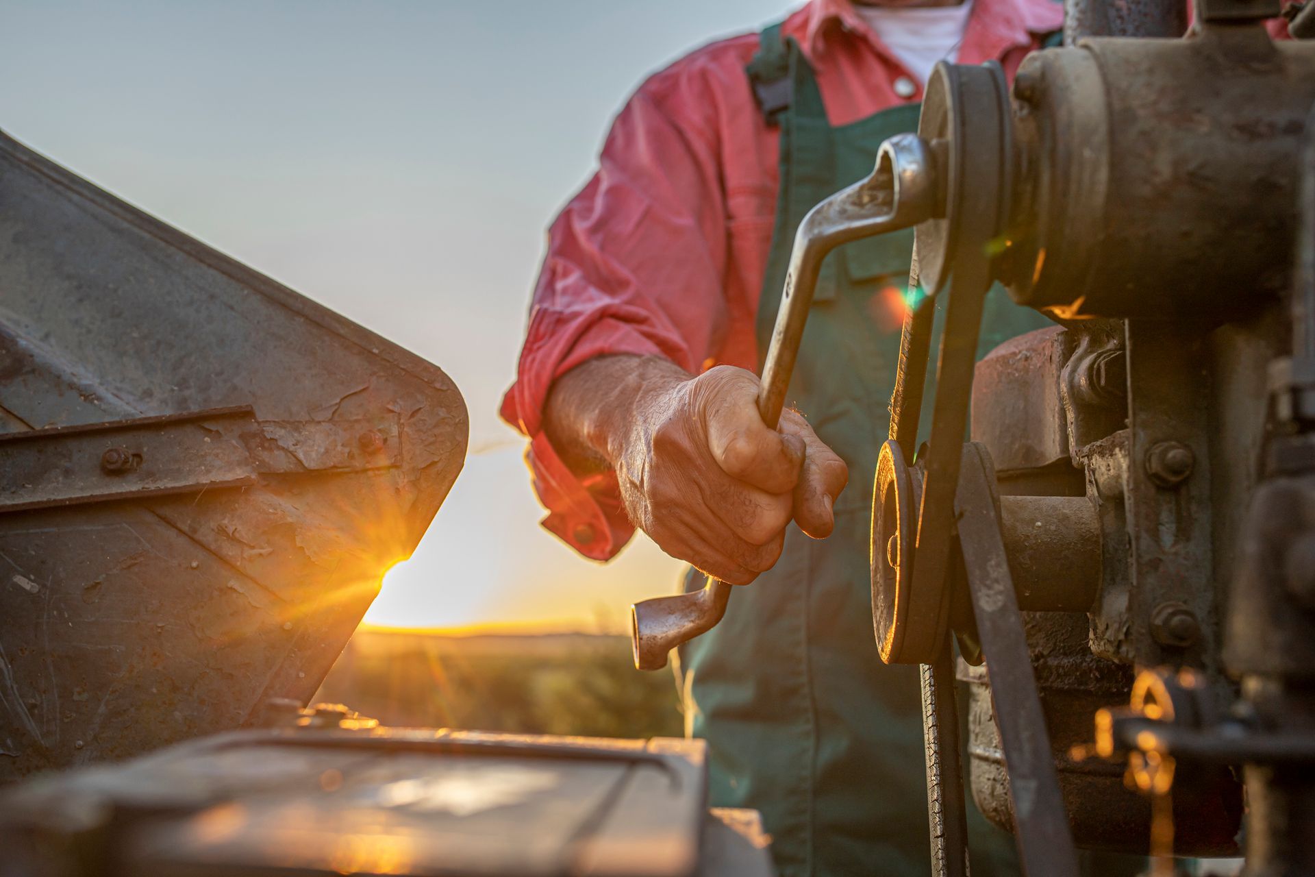 Farmer operating machinery, using a wrench. Sunset in the background.