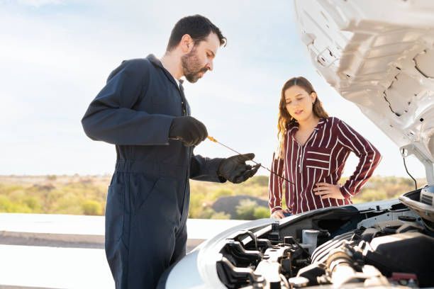 Mechanic checking car's oil with customer observing near an open hood on a sunny day.
