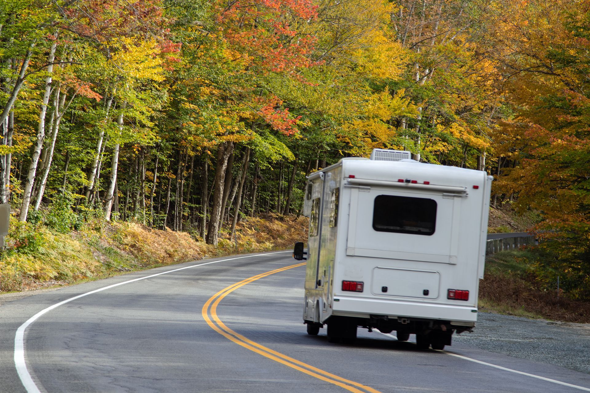 RV driving on a winding road through autumn foliage.