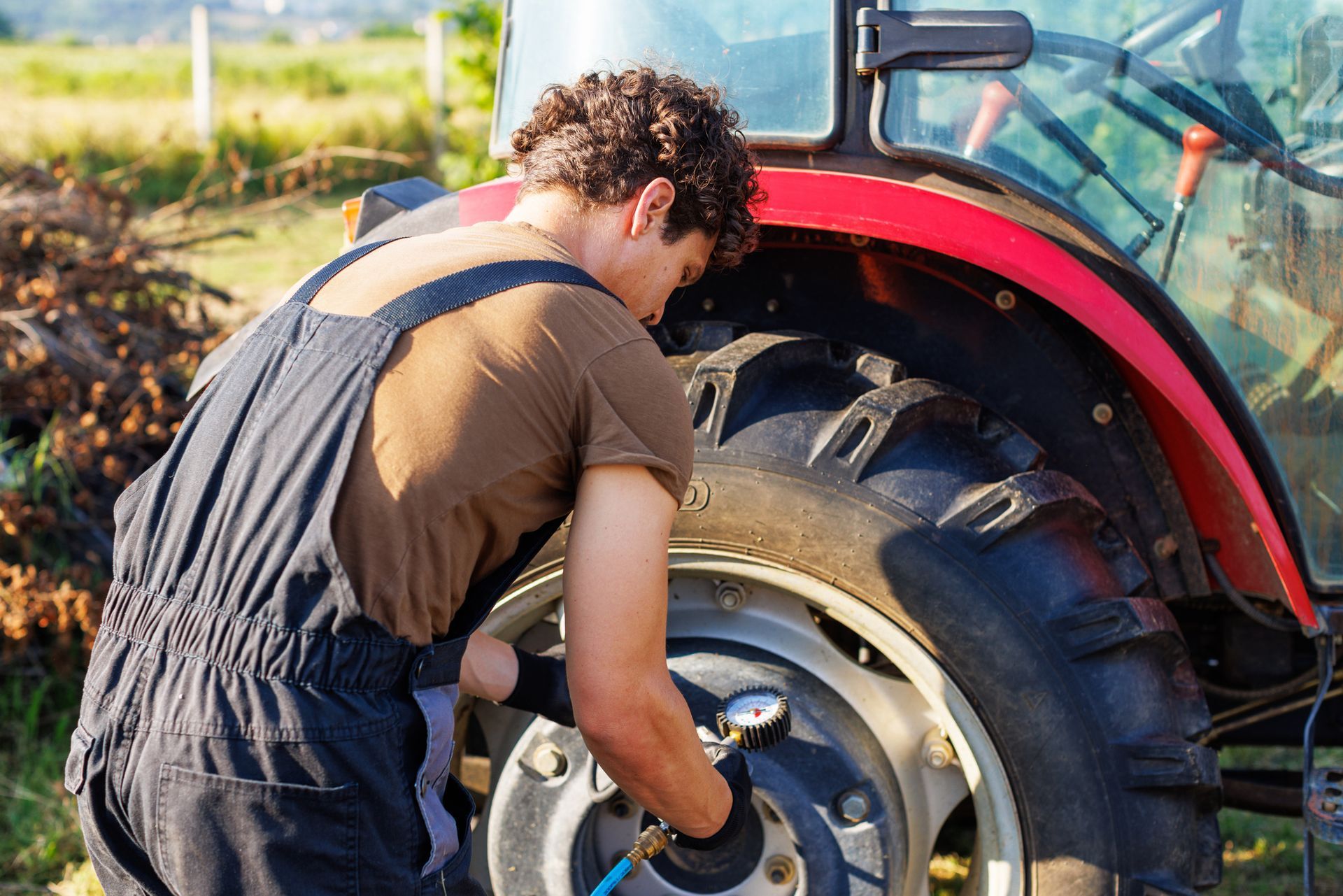 Person in overalls inflating a tractor tire outdoors.
