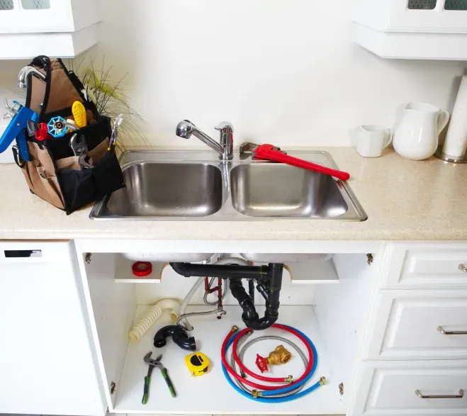 Plumbing tools arranged in and around a kitchen sink, including a toolbox and replacement hoses.