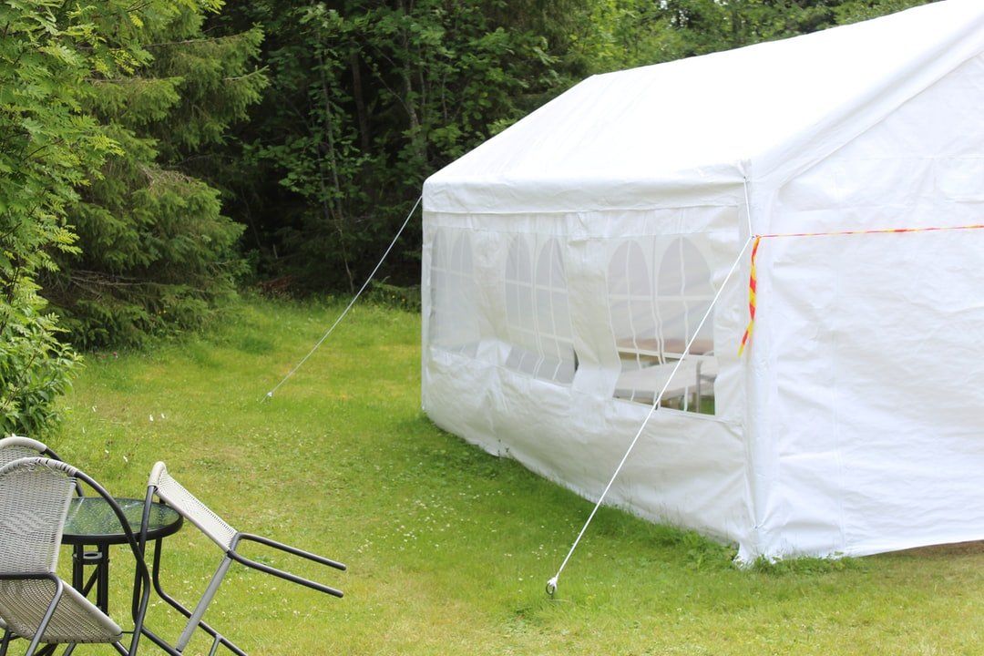 A White Tent Is Sitting In The Grass Next To A Table And Chairs — Grafton Hire In South Grafton, NSW