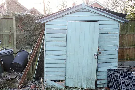 A small blue shed is sitting next to a wooden fence.