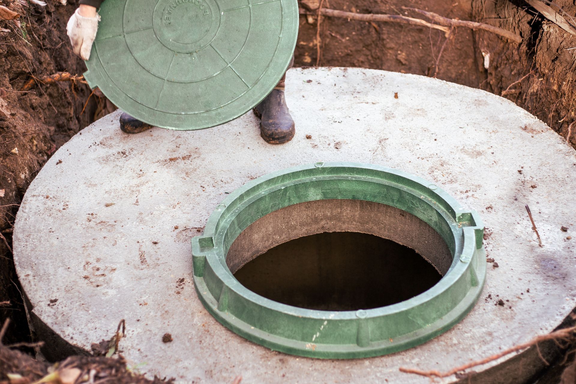 A man is standing next to a manhole cover in the dirt.