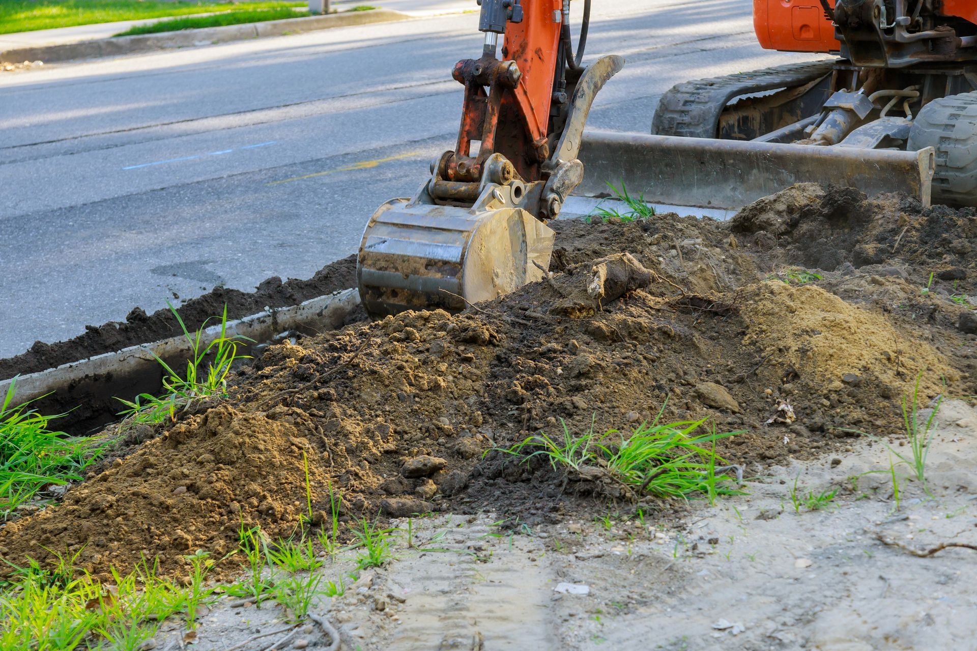 An excavator is digging a hole in the ground next to a road.