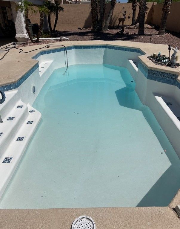 A rectangular swimming pool with blue tiles and light blue water, in a sunny outdoor setting.