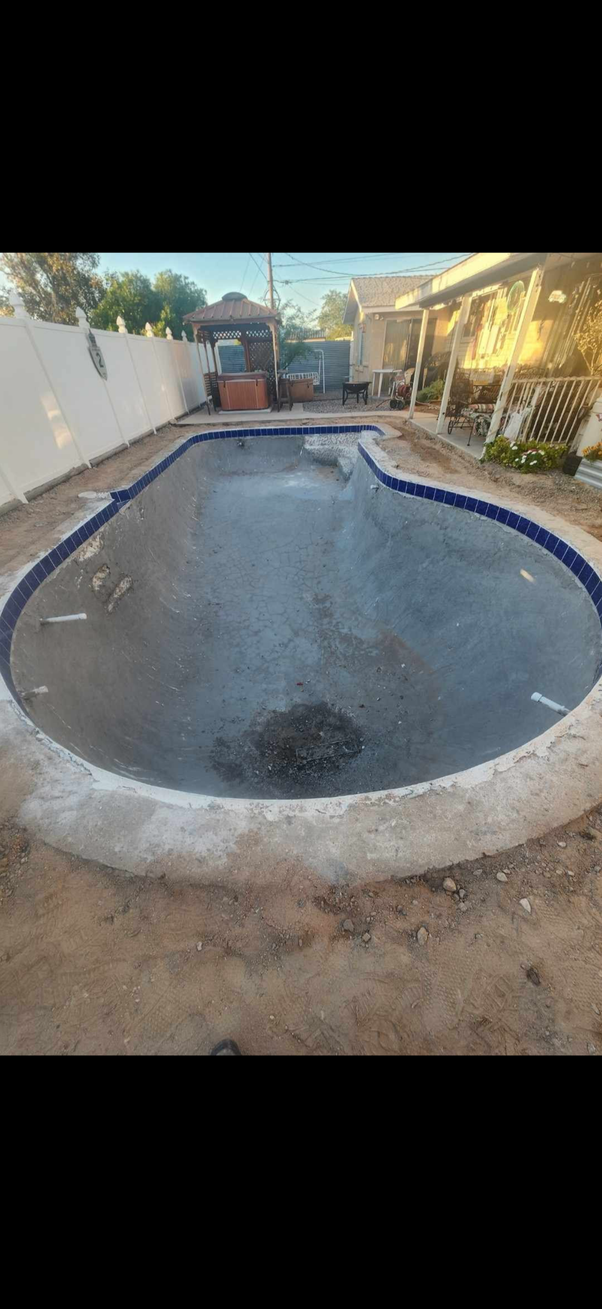 Swimming pool in front of a white villa with a tiled roof, surrounded by lush greenery and palm trees under a blue sky.