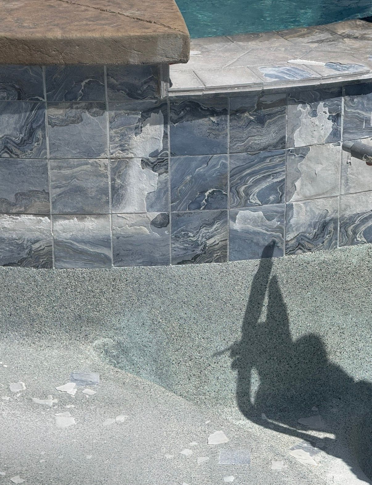 Close-up of a pool's edge with dark, patterned tiles and a textured, light-colored interior.