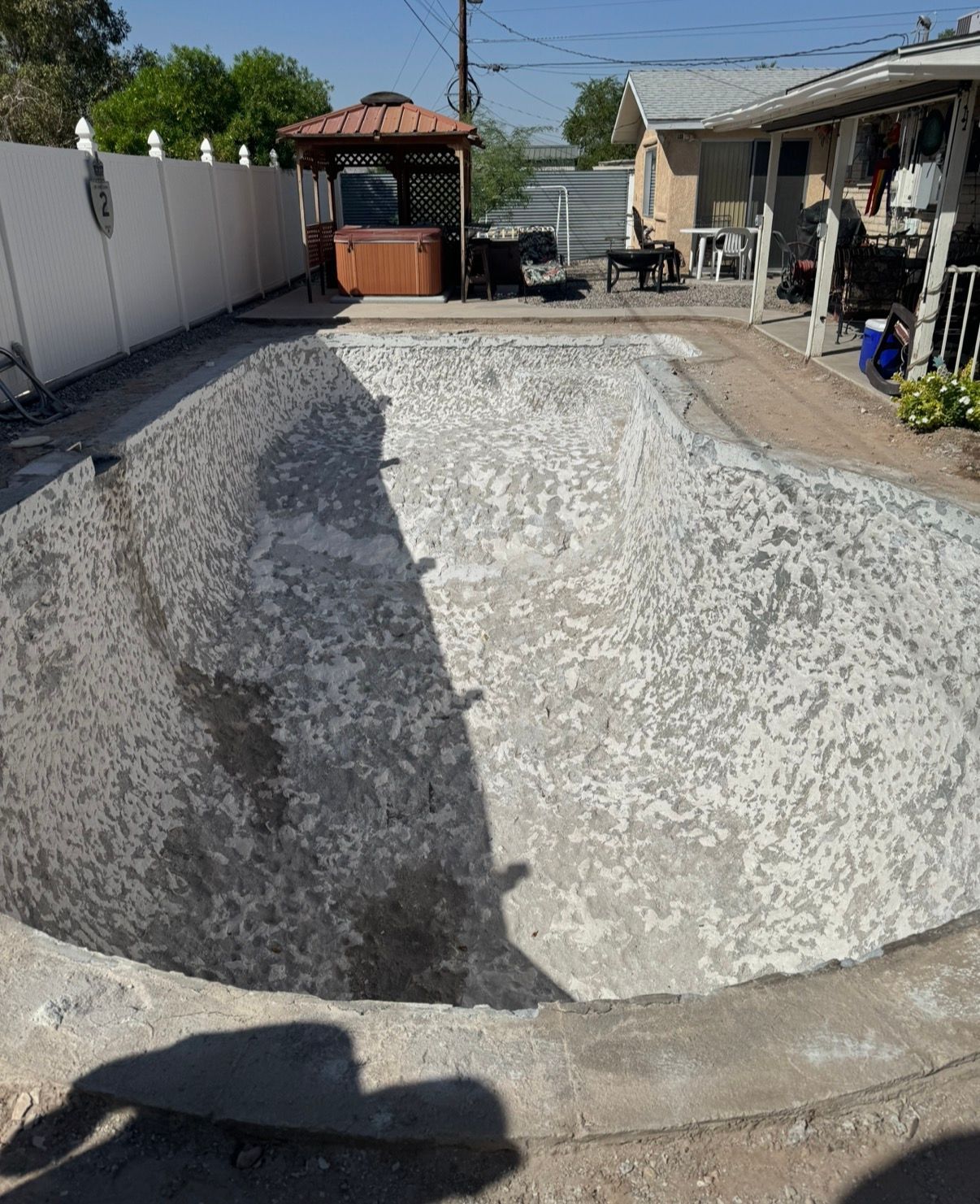 Empty swimming pool, unfinished concrete surface. Backyard setting with gazebo and house.