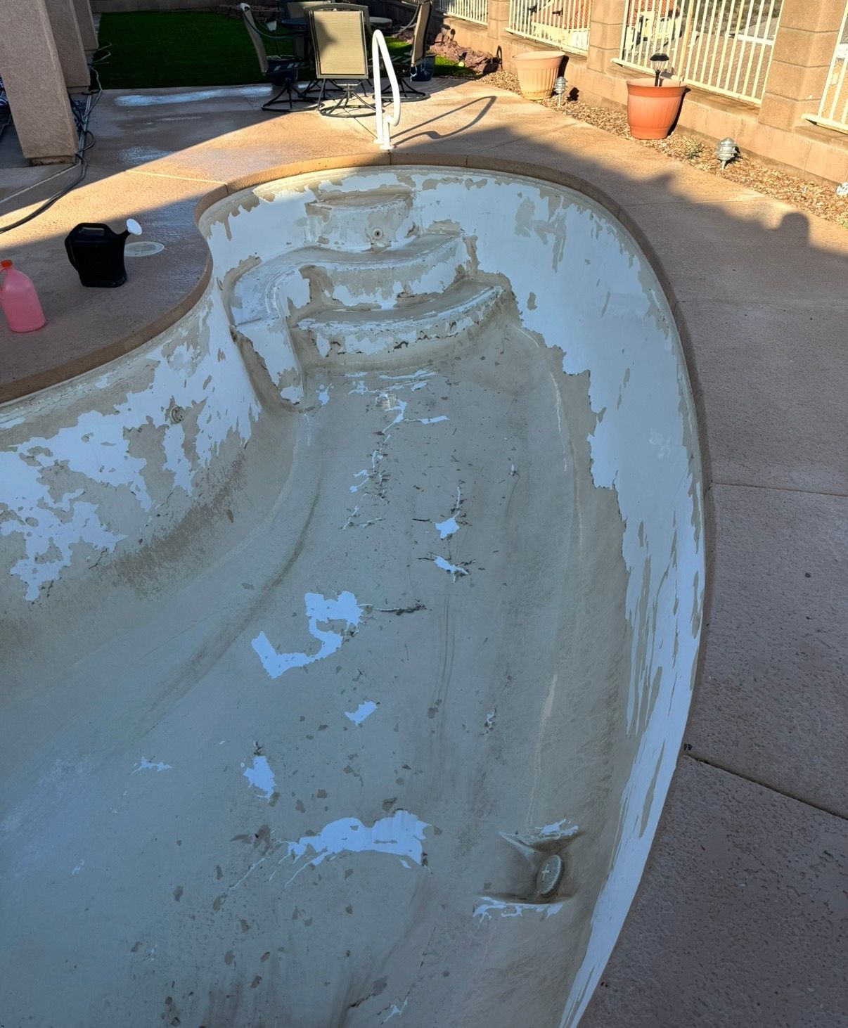 Empty, peeling swimming pool; beige interior, concrete steps, and surrounding patio.