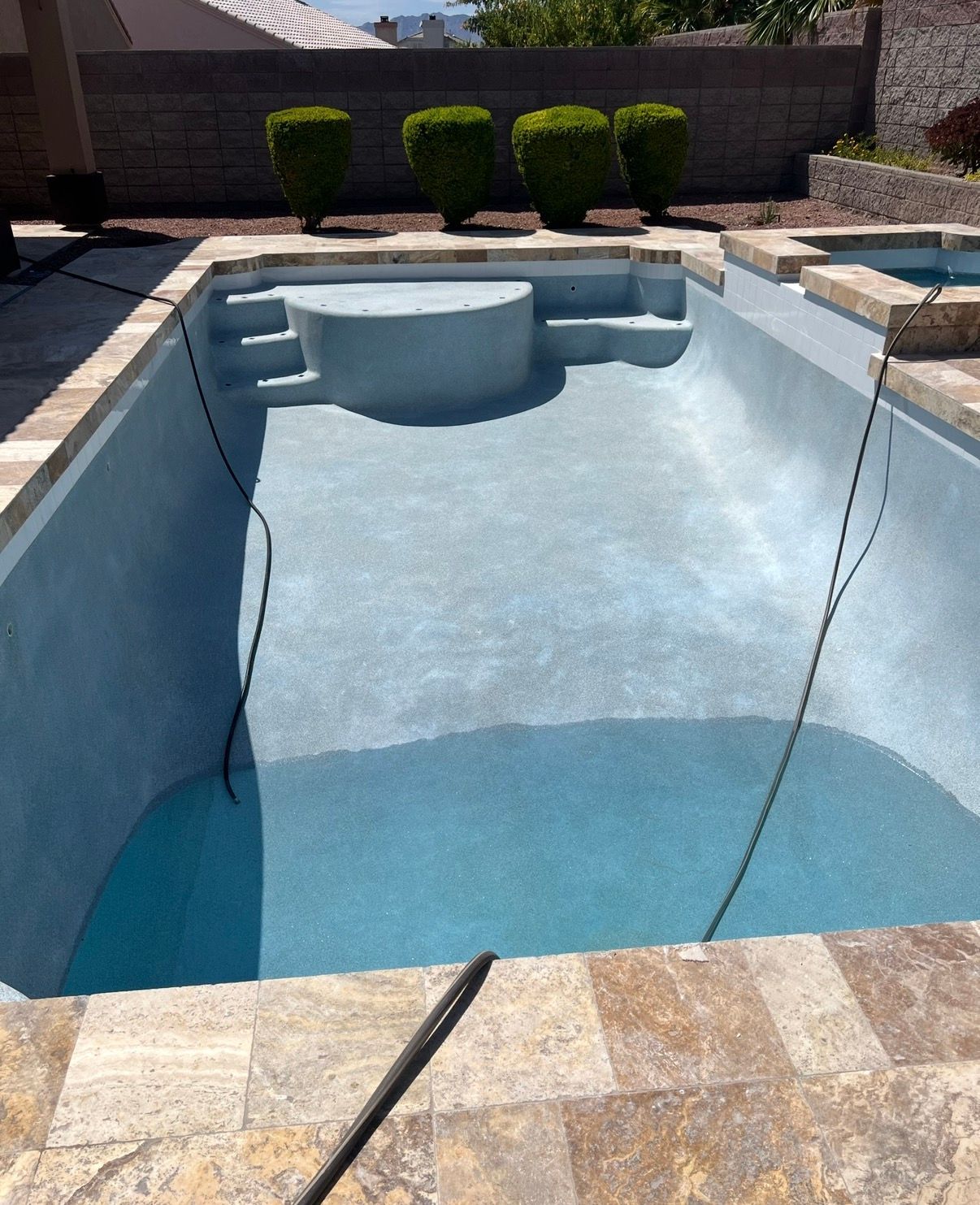 Empty light blue swimming pool with a circular shallow area, set in a stone patio.
