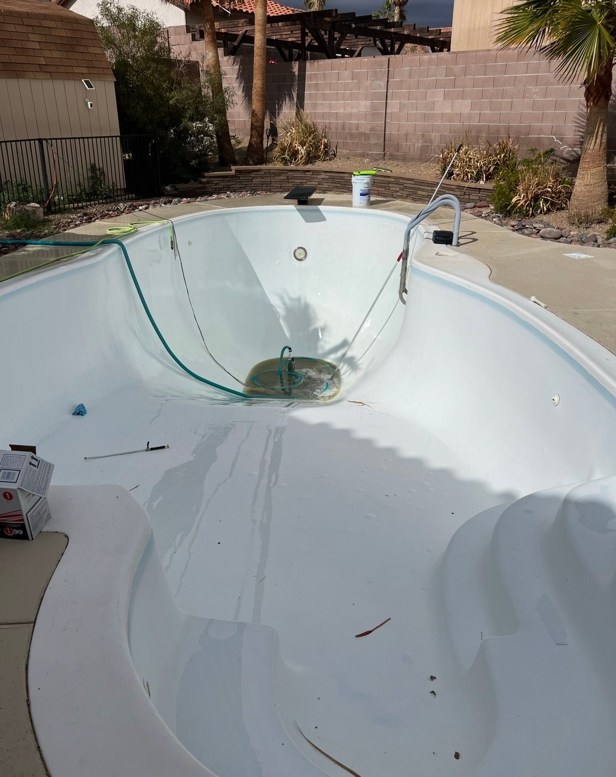 Empty, light blue pool with a few hoses and equipment on the deck, a sunny outdoor scene.