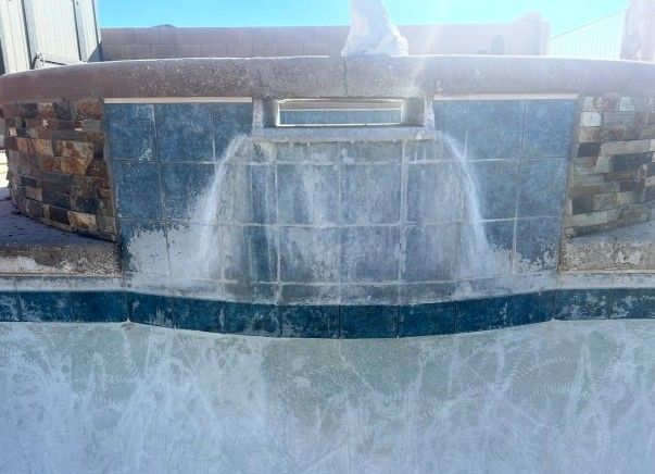 Pool with waterfall feature, blue tile and stone surround, water cascading down.