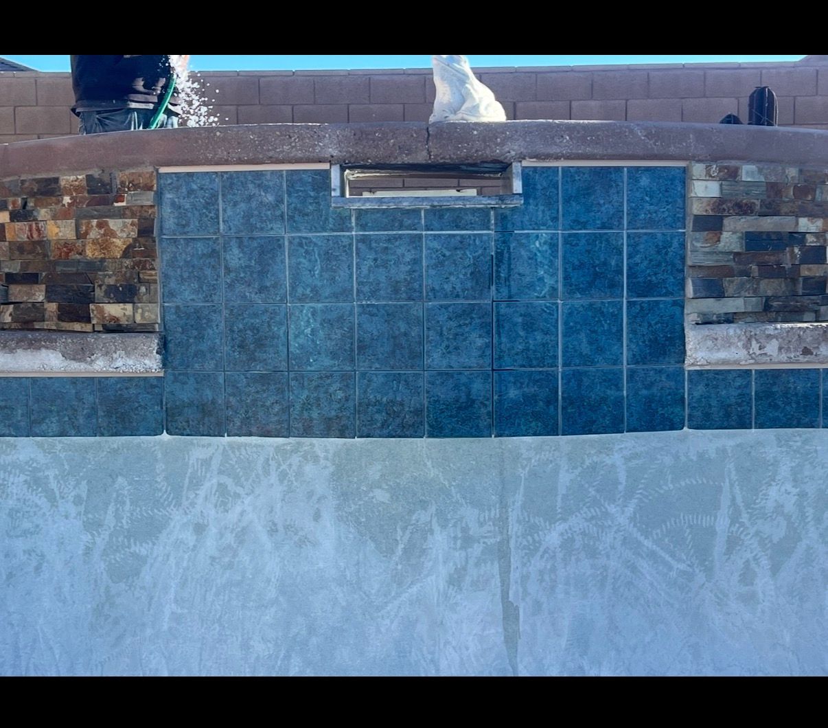 Pool construction: blue tiles installed around a skimmer, with decorative rock and unfinished pool walls.