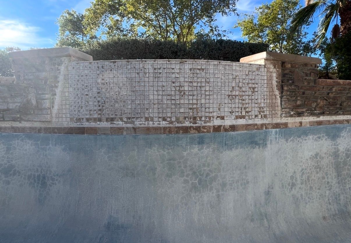 Waterfall feature in a pool, with a brick wall and clear water.