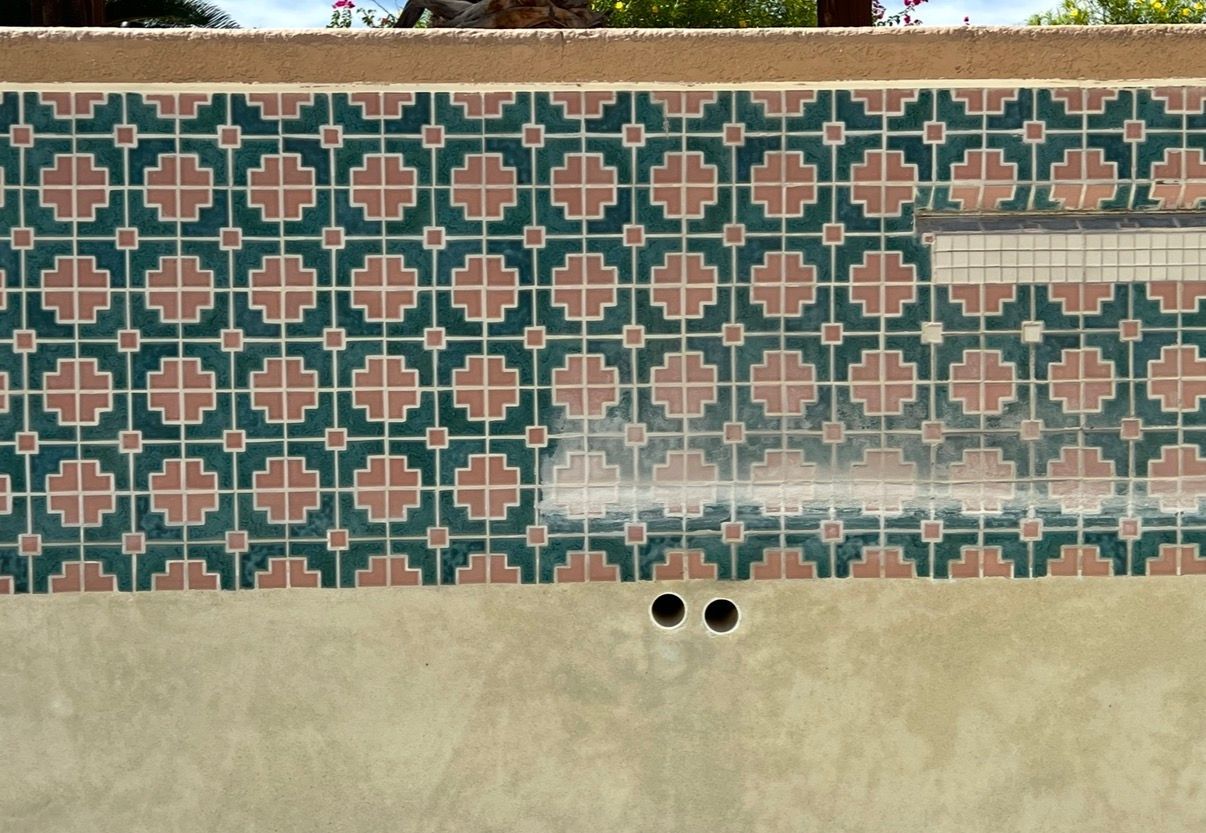 Pool wall with green, pink, and white patterned tile being cleaned with spray.