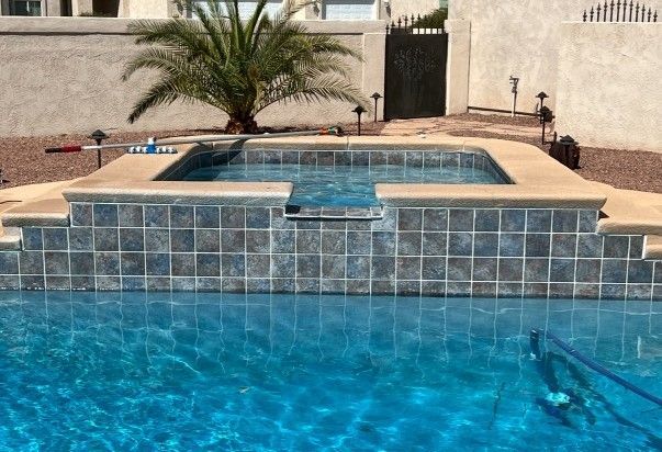 Pool with blue water and a raised hot tub area with tiled walls; outdoors.