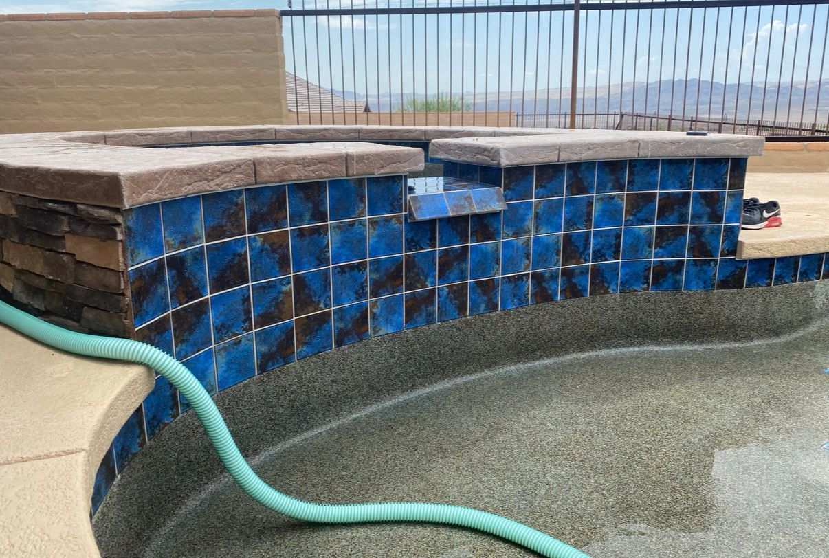 Blue tiled pool feature with dark tiles, water, and a green hose.
