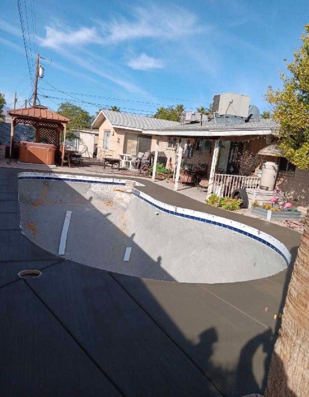 Empty pool with concrete surround, backyard setting with house and gazebo.