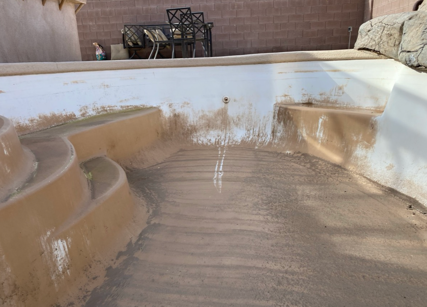 Empty, dirty swimming pool needing cleaning; concrete steps and beige/white interior.
