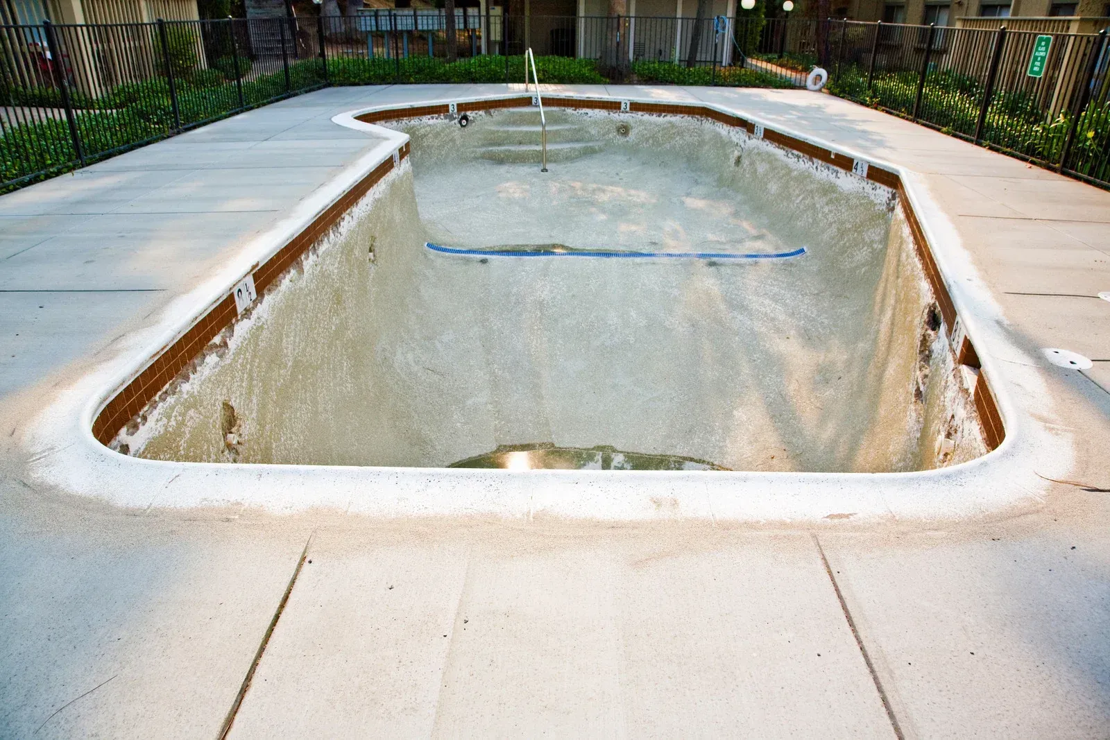 Empty swimming pool with light brown interior and light gray concrete surrounding.