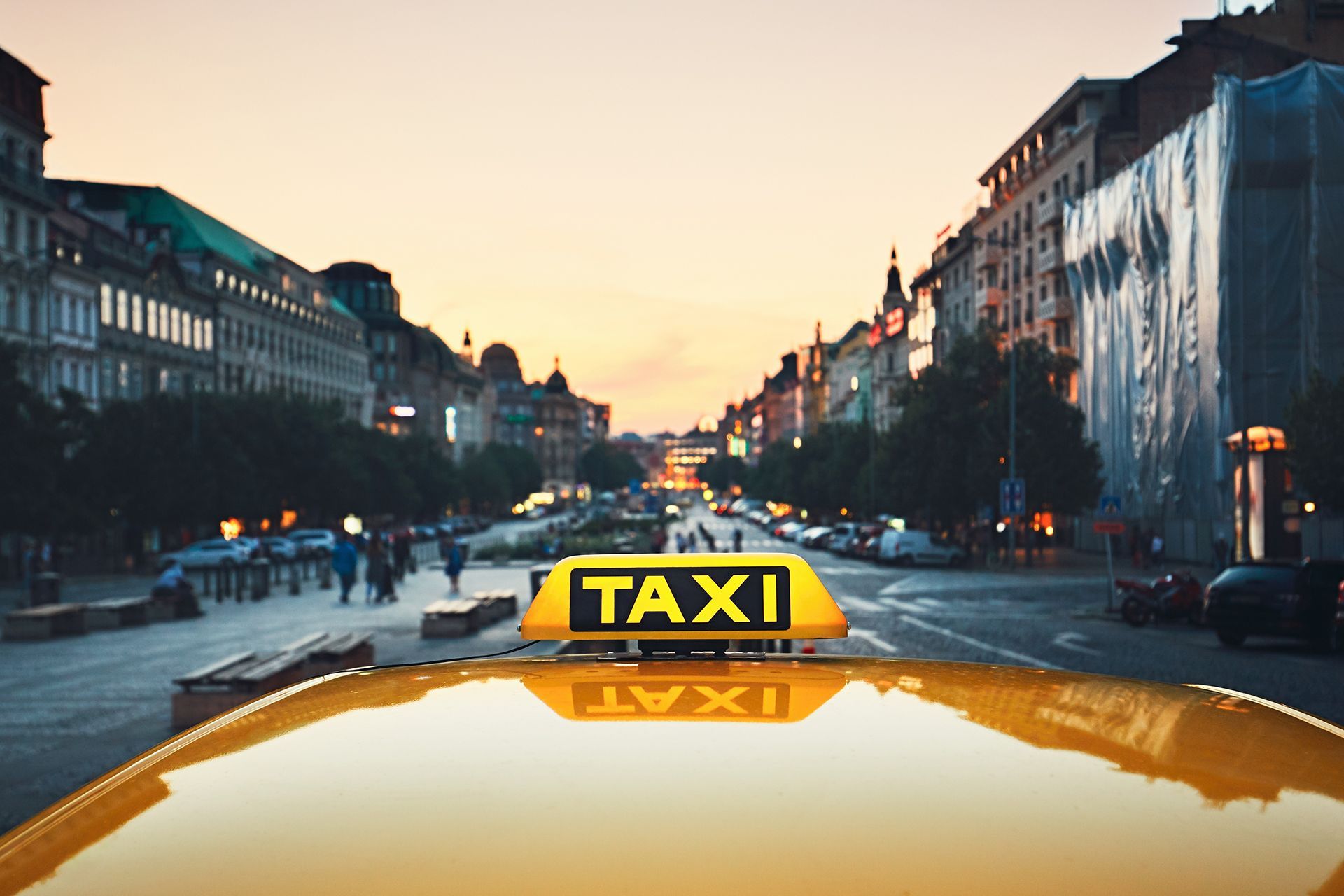 A taxi is driving down a city street at sunset.