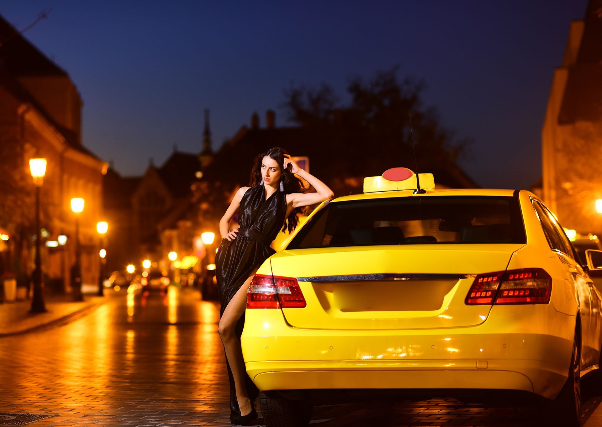 A woman is standing next to a yellow taxi on a city street at night.