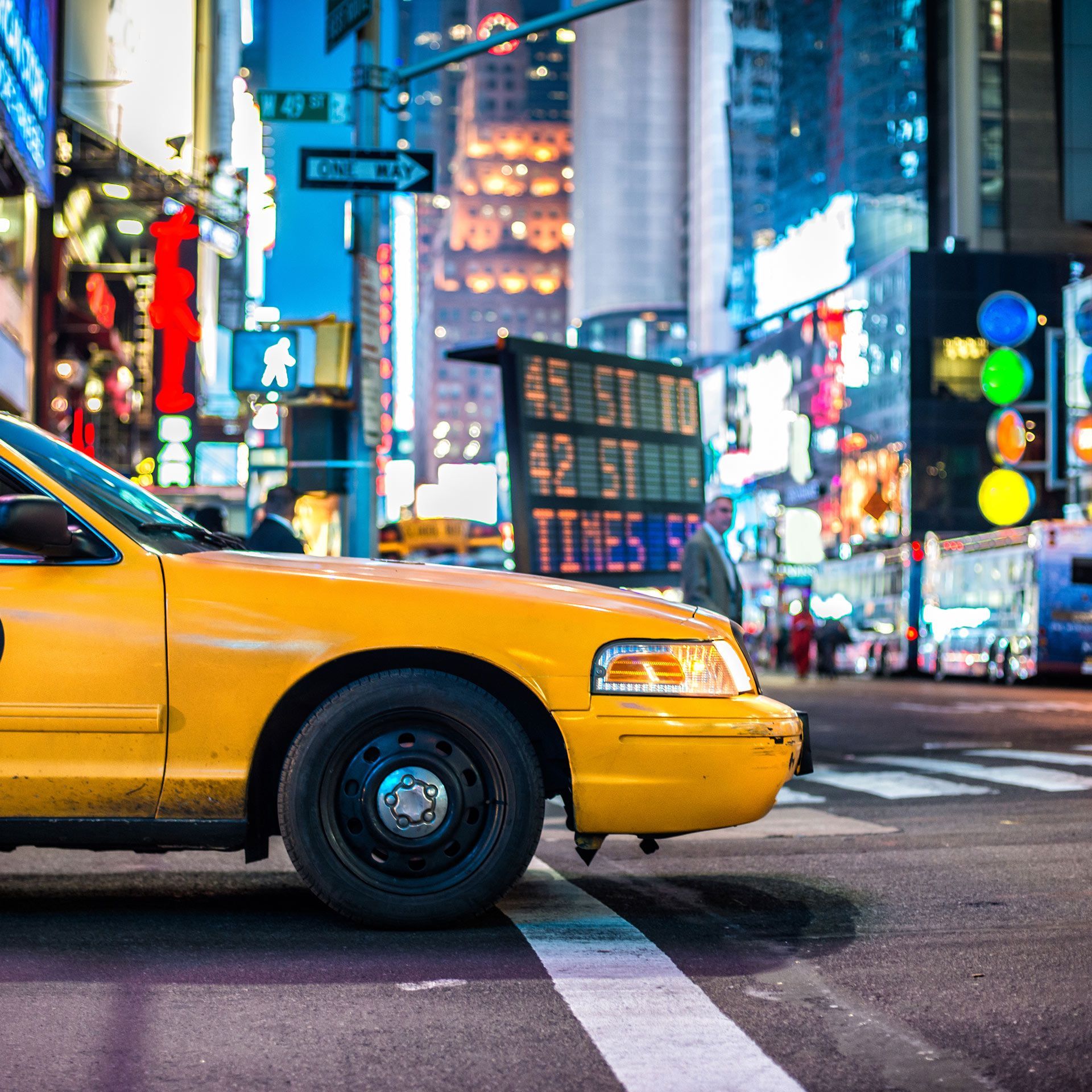 A yellow taxi is driving down a city street at night