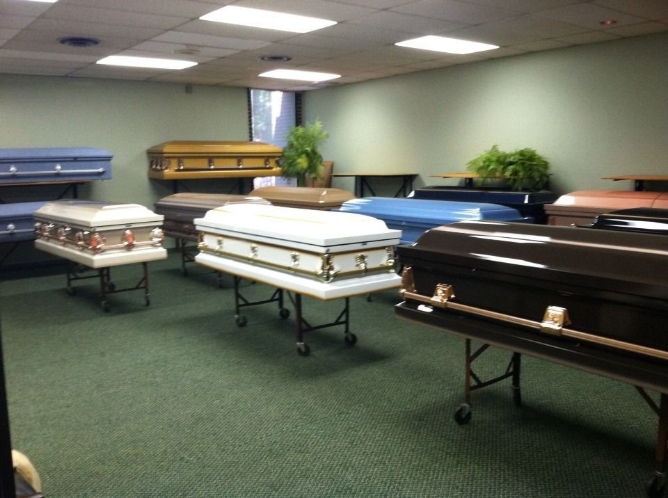 A room with several displayed coffins in various colors and designs on wheeled stands.