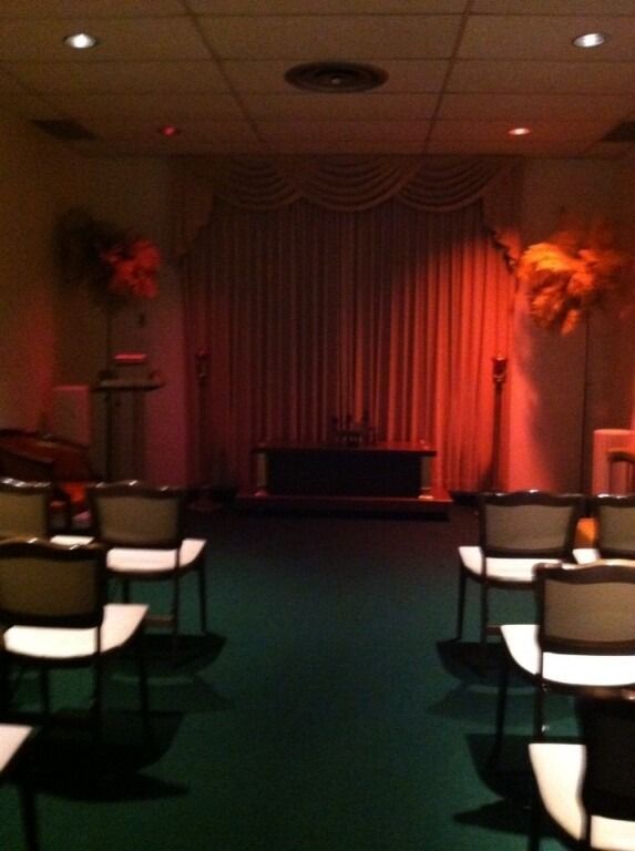 Rows of chairs face a stage with curtains in a dimly lit room; red-orange lighting.
