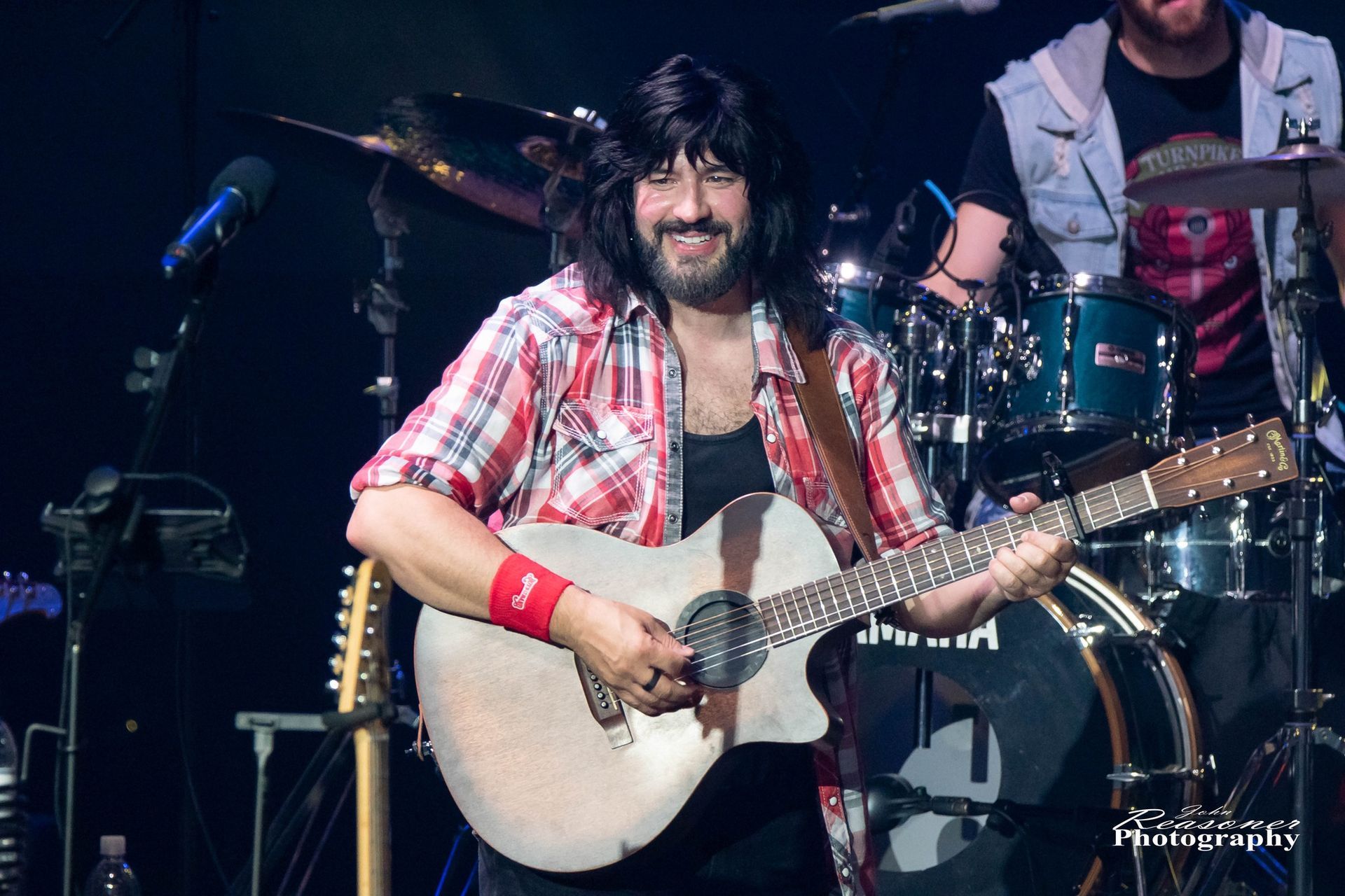 A man with a beard is playing an acoustic guitar on a stage.