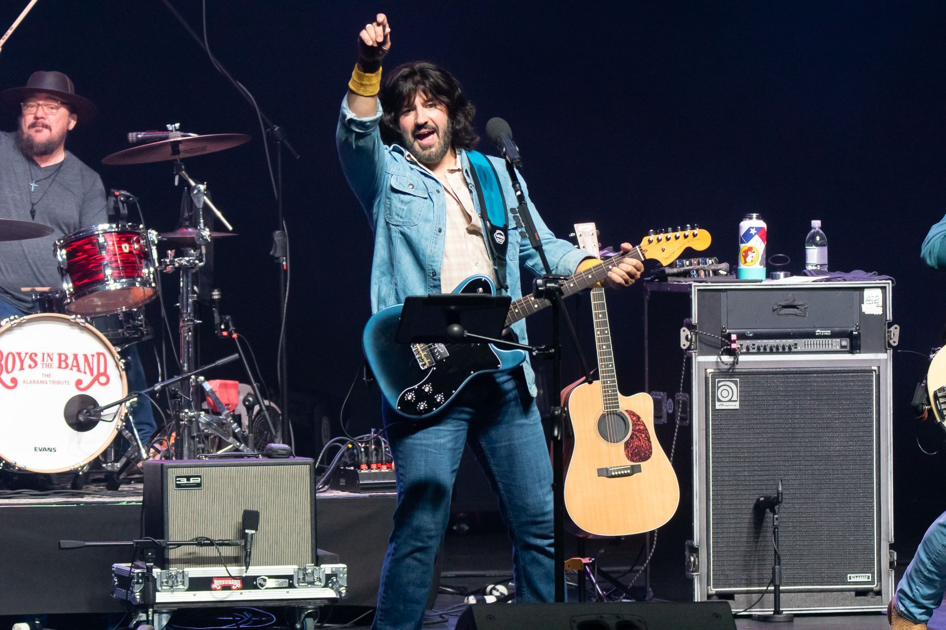 A man playing a guitar in front of a drum set that says jesus band