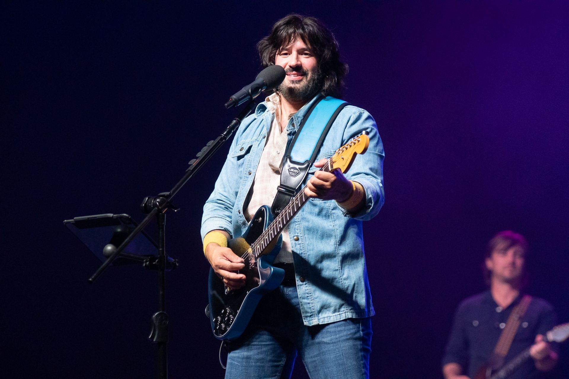 A man is playing a guitar and singing into a microphone on a stage.